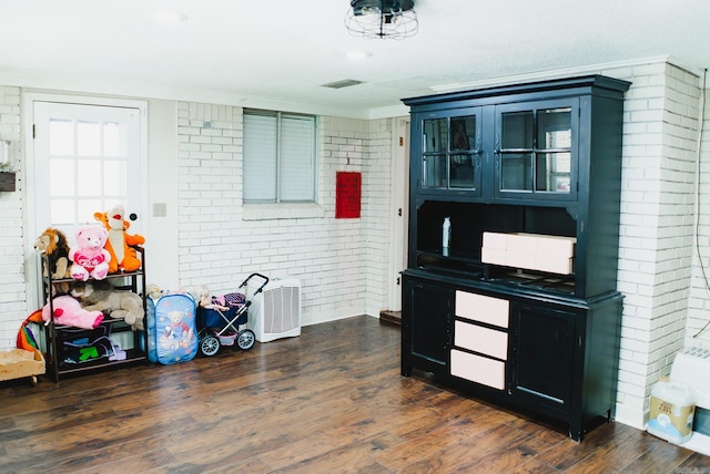 interior space featuring dark hardwood / wood-style flooring, crown molding, and brick wall