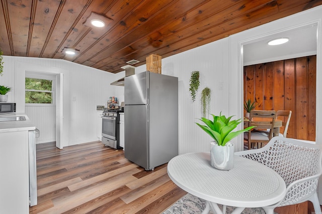 kitchen featuring wood ceiling, wooden walls, appliances with stainless steel finishes, light hardwood / wood-style floors, and lofted ceiling