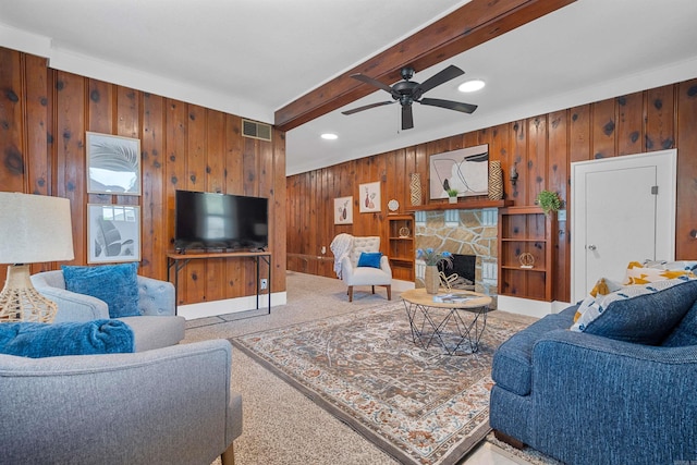 living room with a fireplace, beamed ceiling, wooden walls, ceiling fan, and light colored carpet