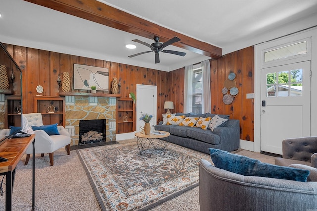 living room featuring ceiling fan, beamed ceiling, wooden walls, a fireplace, and carpet floors