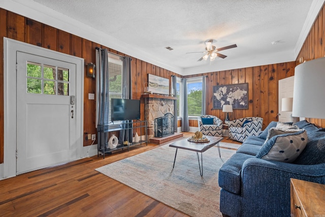 living room featuring a fireplace, a textured ceiling, wooden walls, wood-type flooring, and ceiling fan