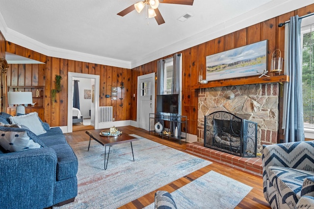 living room featuring ceiling fan, a stone fireplace, wooden walls, hardwood / wood-style floors, and ornamental molding