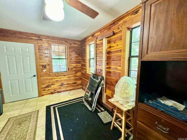 office area with ceiling fan, a wealth of natural light, light tile patterned floors, and wooden walls