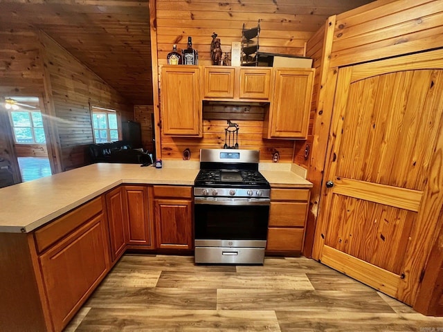 kitchen featuring wooden walls, gas range, light hardwood / wood-style floors, and lofted ceiling