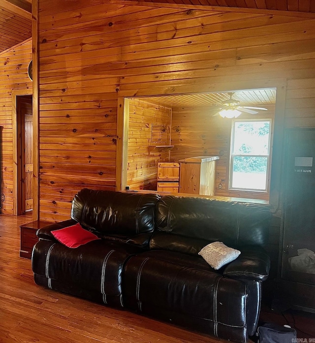 living area featuring a ceiling fan, vaulted ceiling, wood walls, and wood finished floors