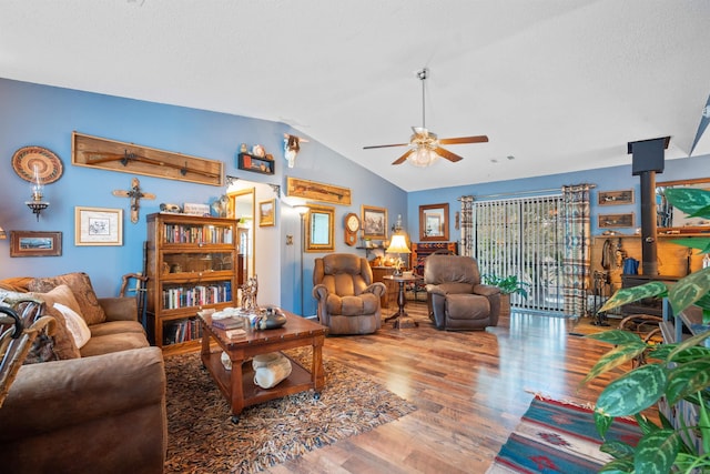 living room featuring ceiling fan, a wood stove, vaulted ceiling, and wood-type flooring