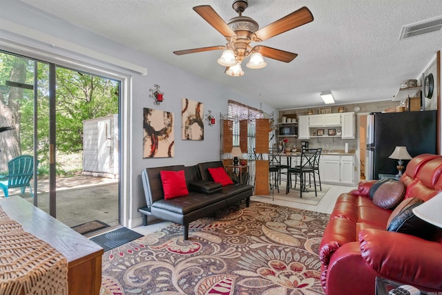 living room featuring ceiling fan, a textured ceiling, and light tile patterned floors