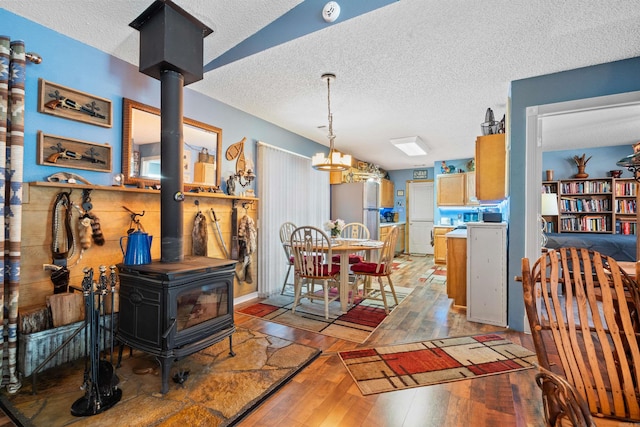 dining room featuring light wood-type flooring, a textured ceiling, a notable chandelier, and a wood stove