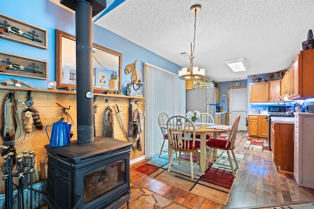 dining room with a textured ceiling, a notable chandelier, hardwood / wood-style floors, and a wood stove