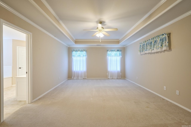 empty room with a tray ceiling, ceiling fan, light colored carpet, and ornamental molding