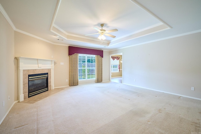 unfurnished living room featuring light carpet, a tile fireplace, a raised ceiling, crown molding, and ceiling fan