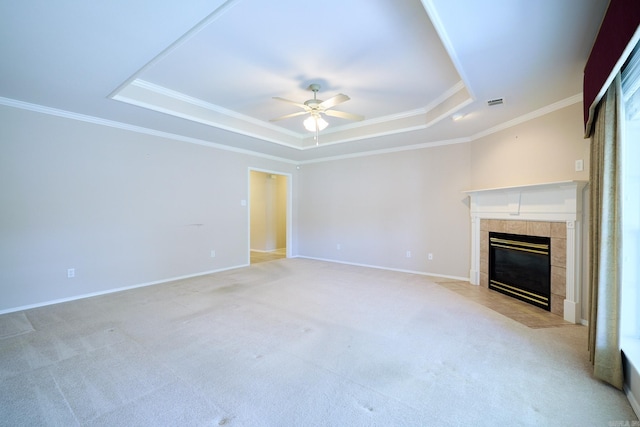 unfurnished living room with a tile fireplace, ceiling fan, light colored carpet, a tray ceiling, and ornamental molding