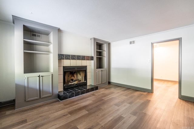 unfurnished living room with hardwood / wood-style flooring, a tiled fireplace, built in features, and ornamental molding