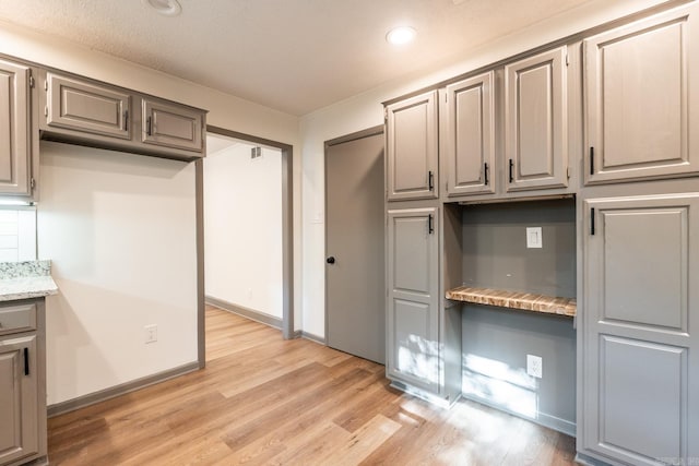 kitchen featuring light hardwood / wood-style flooring, light stone counters, and gray cabinets