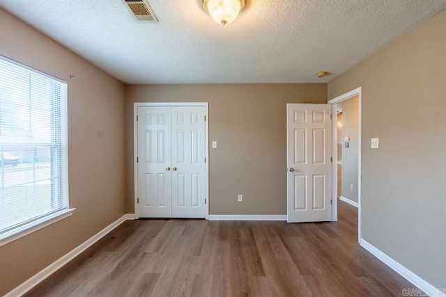 unfurnished bedroom with hardwood / wood-style floors, a closet, and multiple windows