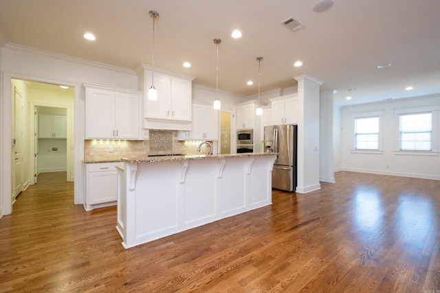 kitchen with backsplash, a kitchen island with sink, hardwood / wood-style floors, appliances with stainless steel finishes, and light stone countertops