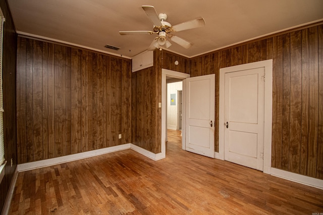 unfurnished bedroom featuring wood walls, ceiling fan, and hardwood / wood-style floors