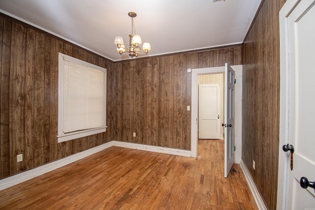 unfurnished room with light hardwood / wood-style flooring, wooden walls, and a notable chandelier