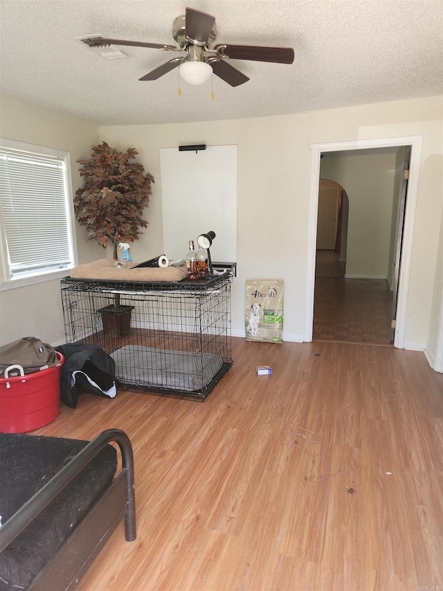 living area with a textured ceiling, ceiling fan, and light wood-type flooring