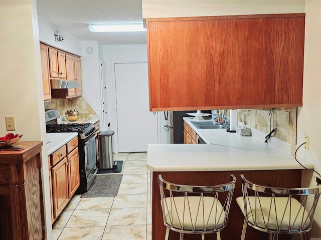 kitchen featuring stainless steel gas range oven, under cabinet range hood, a peninsula, light countertops, and a kitchen bar