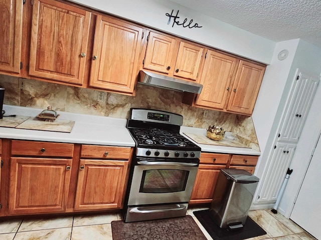 kitchen with stainless steel gas stove, brown cabinetry, light countertops, a textured ceiling, and under cabinet range hood