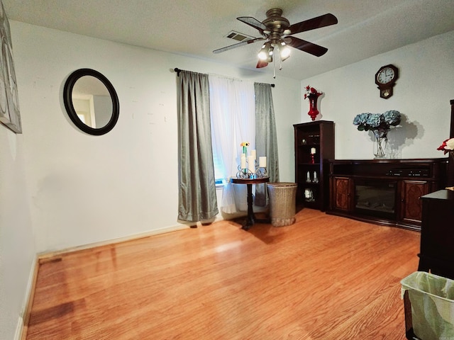 interior space with light wood-type flooring, a glass covered fireplace, baseboards, and a ceiling fan