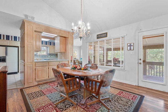 dining area with a notable chandelier, lofted ceiling, and light wood-type flooring
