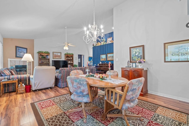 dining room with a towering ceiling, wood finished floors, baseboards, and ceiling fan with notable chandelier