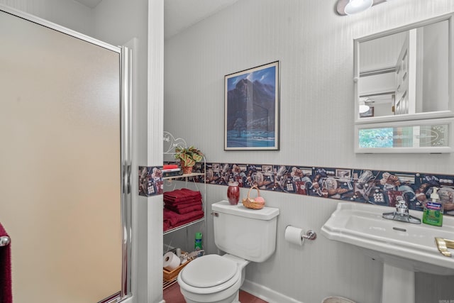 full bath featuring a sink, a shower stall, toilet, a wainscoted wall, and wallpapered walls