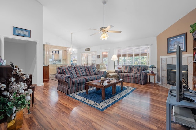 living room with lofted ceiling, wood finished floors, a fireplace, and ceiling fan with notable chandelier