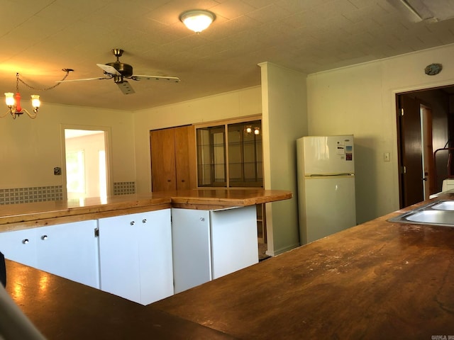 kitchen with ceiling fan with notable chandelier, sink, white refrigerator, and white cabinets