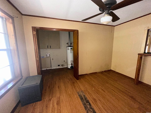 empty room with a wealth of natural light, ceiling fan, water heater, and wood-type flooring