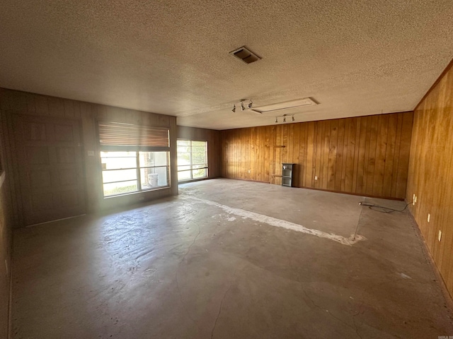 unfurnished room with concrete floors, rail lighting, a textured ceiling, and wooden walls