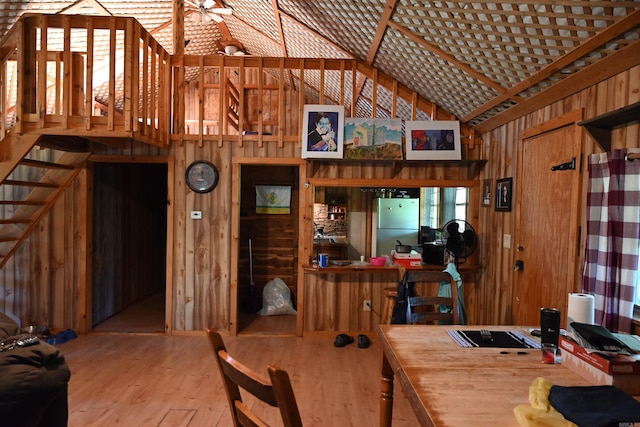 dining area with wood walls, light hardwood / wood-style flooring, and high vaulted ceiling