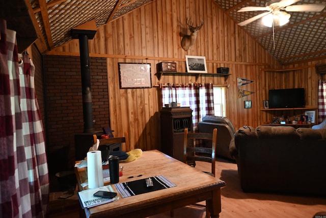 dining room featuring hardwood / wood-style floors, a wood stove, wooden walls, lofted ceiling, and ceiling fan