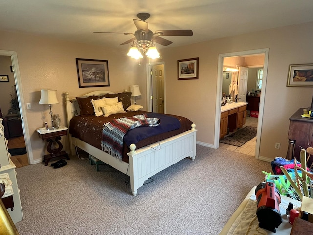 bedroom with ceiling fan, light colored carpet, and ensuite bath