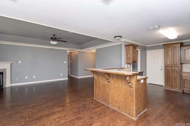 kitchen featuring a kitchen bar, ornamental molding, dark wood-type flooring, ceiling fan, and kitchen peninsula