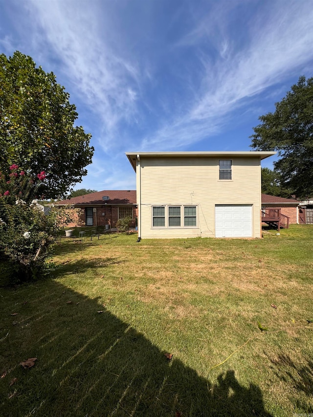 rear view of house featuring a lawn, a garage, and a wooden deck