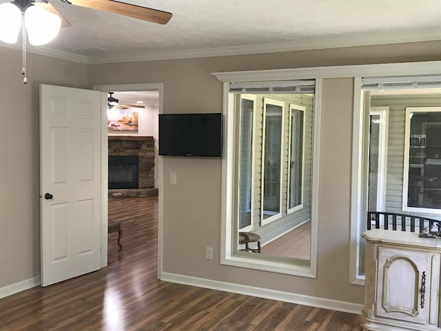 spare room featuring ceiling fan, dark wood-type flooring, crown molding, and a stone fireplace