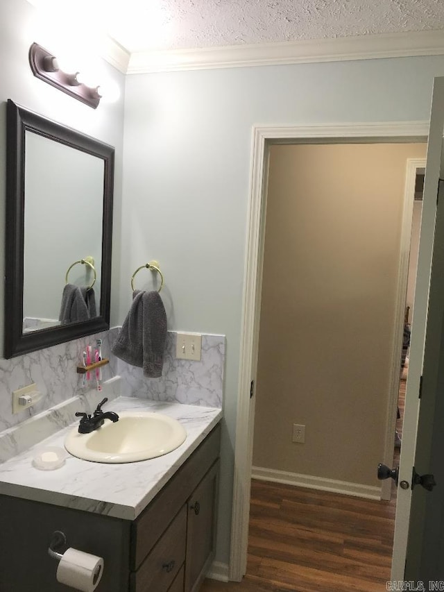 bathroom with wood-type flooring, vanity, a textured ceiling, ornamental molding, and decorative backsplash