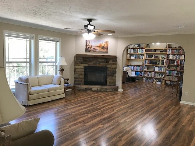 living room with a fireplace, ornamental molding, ceiling fan, a textured ceiling, and dark wood-type flooring