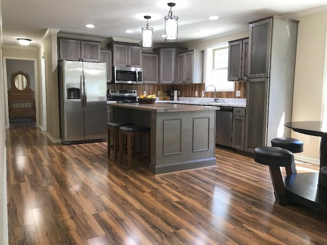 kitchen featuring a kitchen island, dark hardwood / wood-style floors, decorative light fixtures, crown molding, and stainless steel appliances