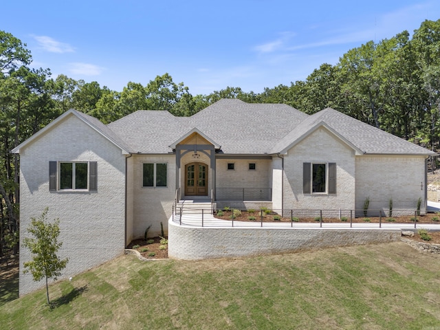 view of front of house with french doors, brick siding, fence, and a front lawn