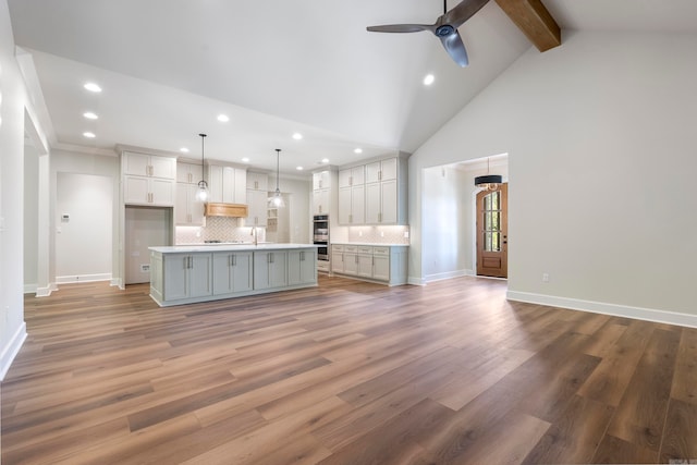 kitchen featuring decorative light fixtures, beam ceiling, light hardwood / wood-style flooring, a kitchen island with sink, and tasteful backsplash