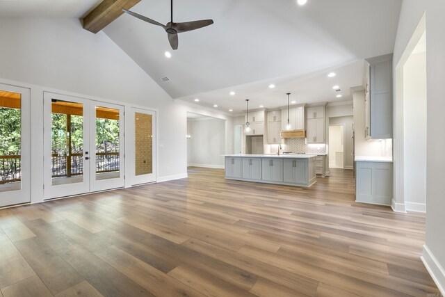 unfurnished living room featuring high vaulted ceiling, beamed ceiling, light hardwood / wood-style flooring, and french doors