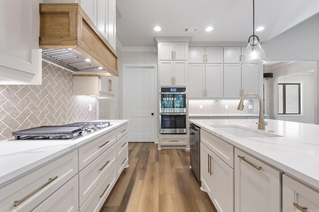 kitchen with sink, hanging light fixtures, light hardwood / wood-style floors, premium range hood, and stainless steel appliances