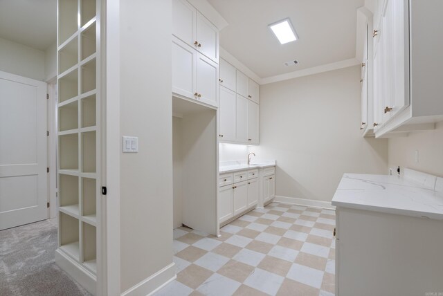 interior space with sink, light stone countertops, light tile patterned floors, crown molding, and white cabinets