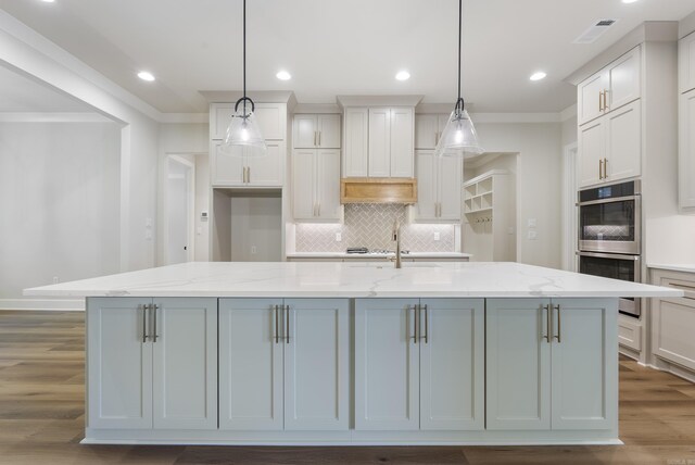 kitchen with light stone counters, a center island with sink, ornamental molding, and light hardwood / wood-style flooring