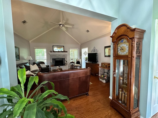 living room with ceiling fan, vaulted ceiling, a stone fireplace, and dark hardwood / wood-style flooring