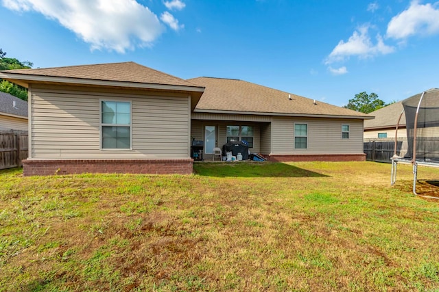 rear view of property featuring a patio, a trampoline, and a yard